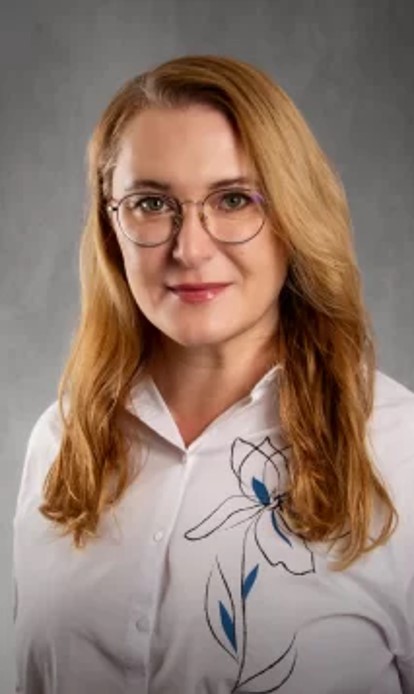 Kobieta z długimi włosami i okularami na twarzy, ubrana w białą koszulę z kwiatowym wzorem.